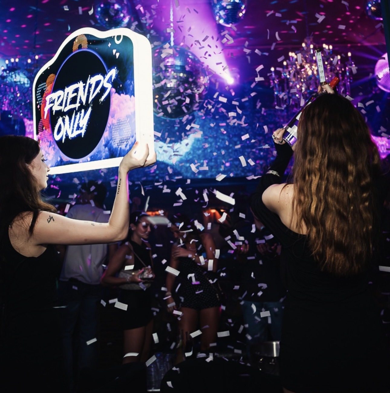A guest holding a lit Friends Only sign in falling confetti